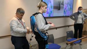 A woman wears an assistive exoskeleton as a man adjusts its straps