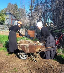 two sisters with shovels and a wheel barrow, loading dirt to move for planting baby pots