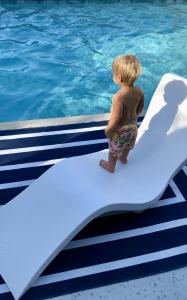 Toddler standing barefoot on a white pool lounger, gazing out over the water — symbolizing future generations and eco-conscious living.