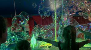 Soap foam in stage light. One girl extends her arms to embrace the bubbles.