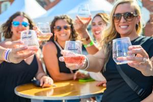 A group of women smile with glasses of wine in a quaint downtown street festival.