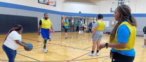 A group of people in yellow jerseys practicing basketball in a gymnasium, with one person preparing to pass a ball.