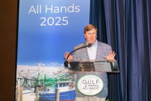 A close-up shot of Mississippi Governor Tate Reeves, standing on stage, speaking to a large crowd of meeting attendees.