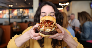 The Extra Napkin Burger at Iron Hill Brewery & Restaurant, available during Burger Month May 23, 2025. The burger includes bacon, coleslaw, fried onion strings, cheddar, and BBQ sauce.