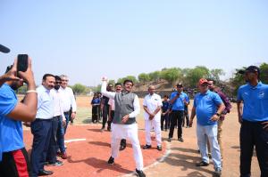  On a baseball field, Shri Bharat Singh Kushwah, Hon’ble Member of Parliament, in a white Indian kurta and grey Nehru Jacket, is poised to throw the ceremonial first pitch.