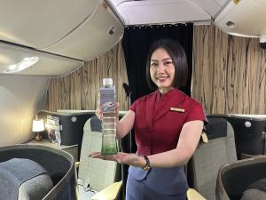 A China Airlines flight attendant in a red uniform smiles while presenting a tall, limited-edition “Taipei 101 Pure Water” bottle inside a Premium Business Class cabin.