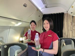 Two China Airlines flight attendants in red uniforms hold bottles of limited-edition “Taipei 101 Pure Water” inside the Premium Business Class cabin.