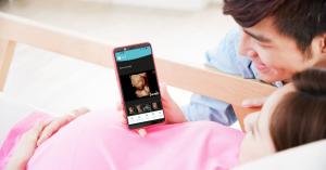 An expectant mother smiles while viewing a 3D ultrasound image on her smartphone, sharing the moment with a loved one.
