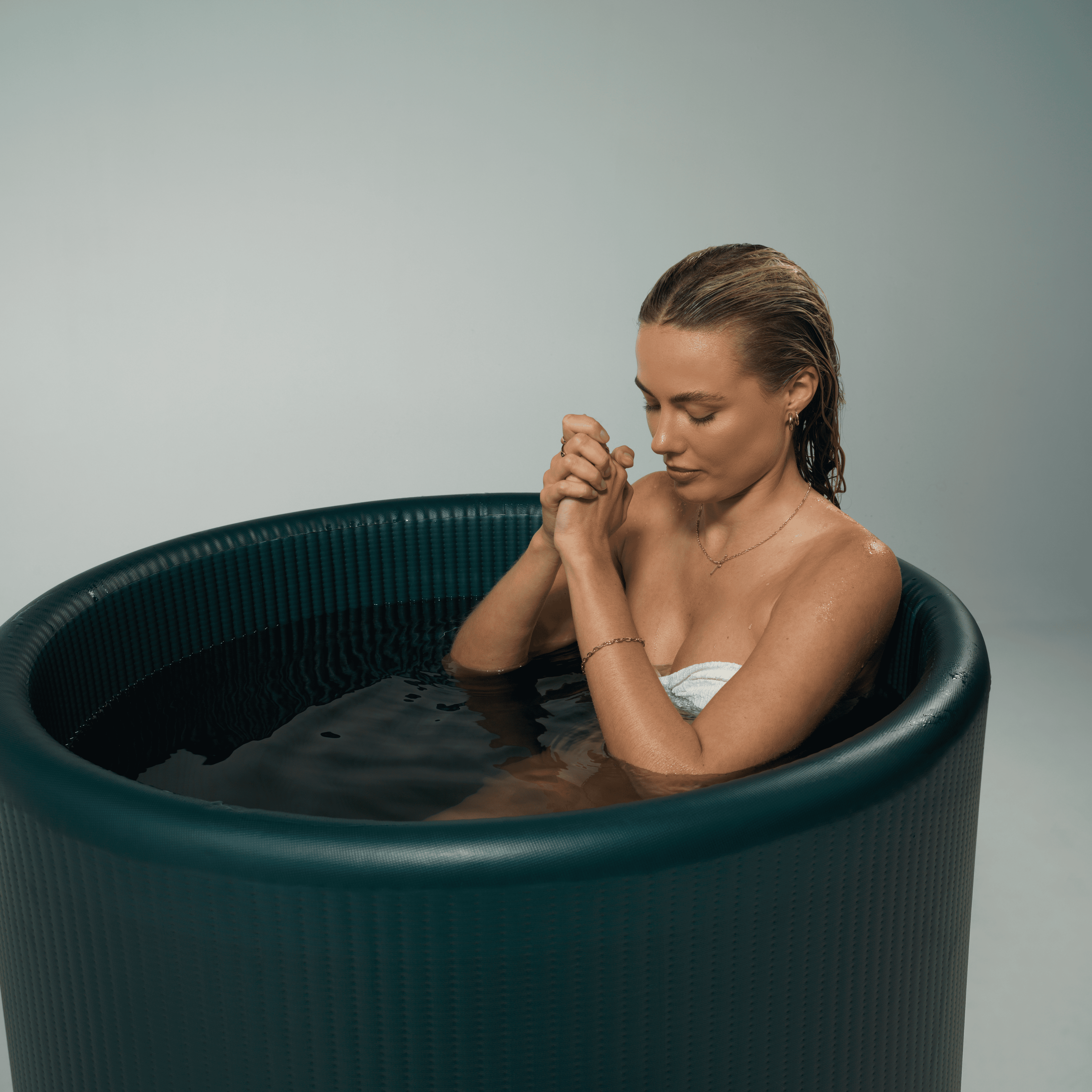 Woman practicing deep breathing while immersed in a dark green/blue cold plunge tub (the water has been cooled by SnowCap's thermoelectric lid technology) by Clearwater Wellness Co.
