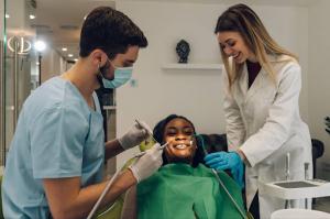 A male dentist provides dental treatment to an African American female patient while his female dental assistant places the air-water syringe in the patient’s mouth.