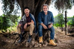 Marcelo Pelleriti y Miguel Priore sentados bajo un olivo en el viñedo Los Pioneros en Mendoza, sosteniendo copas de vino Pelleriti Priore
