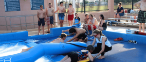 Children enjoy a water activity on an inflatable surface while adults observe from nearby, creating a lively summer atmosphere.