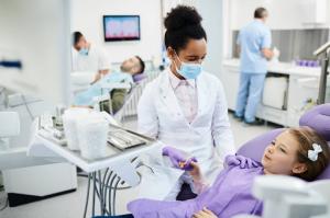 A female pediatric dentist gently reassures a child with a calming touch before a checkup.