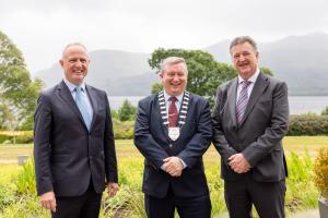 three men in suits smiling with mountain and lake scenery in the background