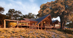 Rendered exterior of Thitaka Lodge at sunset, showing an elevated, thatch-roofed structure with large open-air decks, surrounded by tall trees and golden grassland in Namibia’s Zambezi Region.