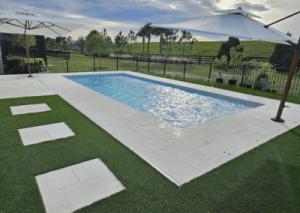 A serene backyard pool with clear blue water, surrounded by a white-tiled deck and green grass.