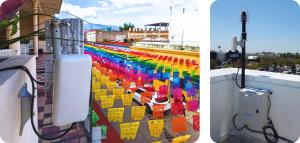 Two rooftop-mounted Wi-Fi installations by LongFi Solutions: one overlooking a colorful pedestrian street in Oaxaca, Mexico, and another on a commercial building near a Lowe’s parking lot in the United States. Both units are equipped with enterprise-grade