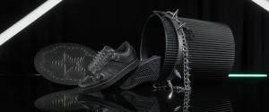 Studio still life of a pair of all-black etnies Hardwired Kingpins surrounded by a spiked chain, metal bin and neon light reflections.