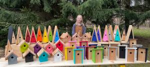 Mia is surrounded by her colorful birdhouse creations.