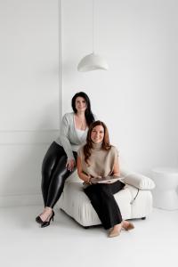 Founders of CoreLife Wellness sitting and standing in a bright, modern studio — leaders in pelvic health, Emsculpt therapy, and women’s wellness in Oakville, Ontario.