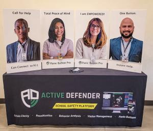 Active Defender event display featuring four large posters showing diverse school staff using the Panic Button Pro system, alongside a branded table promoting school safety features like crisis clarity and visitor management.