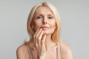 A woman gently touching her face, representing skin care and wellness supported by Aetheion®'s antioxidant-rich formulations.