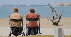 Two elderly adults sitting on their rollator walkers near the ocean, enjoying outdoor summer mobility and scenic water views.