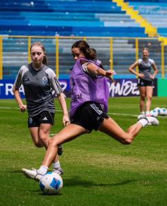 A female soccer player defending the ball, wearing a purple jersey with a white t-shirt underneath and black shorts.