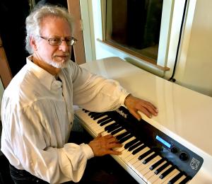 Steven Halpern in white shirt sitting at white piano