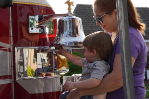 Mother supports toddler ringing a quiet fire-engine bell at Bierman Autism Centers’ sensory-friendly Touch-a-Truck event.