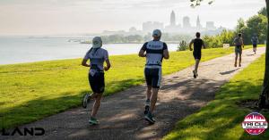 Tri CLE 2023 participants running along a lakeside path with the Cleveland skyline in the background on a sunny morning during the run portion of the race.