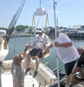 Man seated in Handicaptain lift being gently lowered onto a boat by a team at Dunkirk Pier, demonstrating the ADA-compliant system’s safe and accessible boarding process.