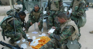 U.S. soldiers in camouflage gear gathering and reading handwritten letters from home while deployed in a desert environment.