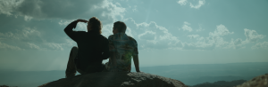 Two characters sit together on a mountaintop, gazing at the vast landscape under a cloudy sky. The scene captures an emotional turning point from Home(sick): A Journey Within, symbolizing connection and self-discovery.