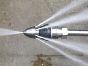 Close-up of a hydro jetting nozzle spraying high-pressure water to clean grease and debris from a pipe.