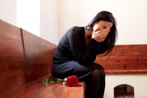 Woman dressed in black sitting in a church pew head low crying, in mourning